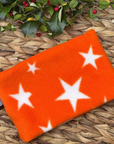 Orange snood with white stars on a woven surface with holly leaves and berries.