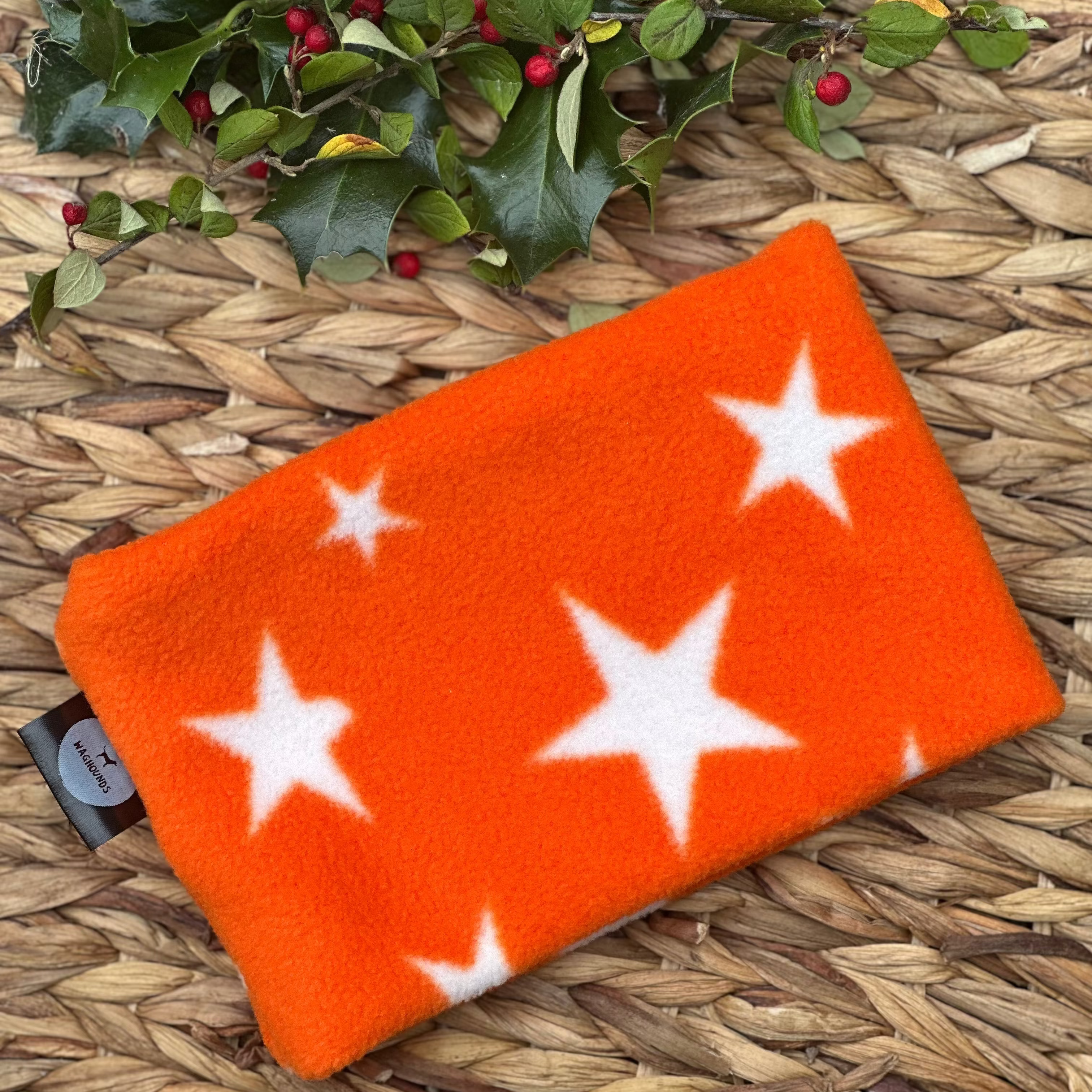 Orange snood with white stars on a woven surface with holly leaves and berries.